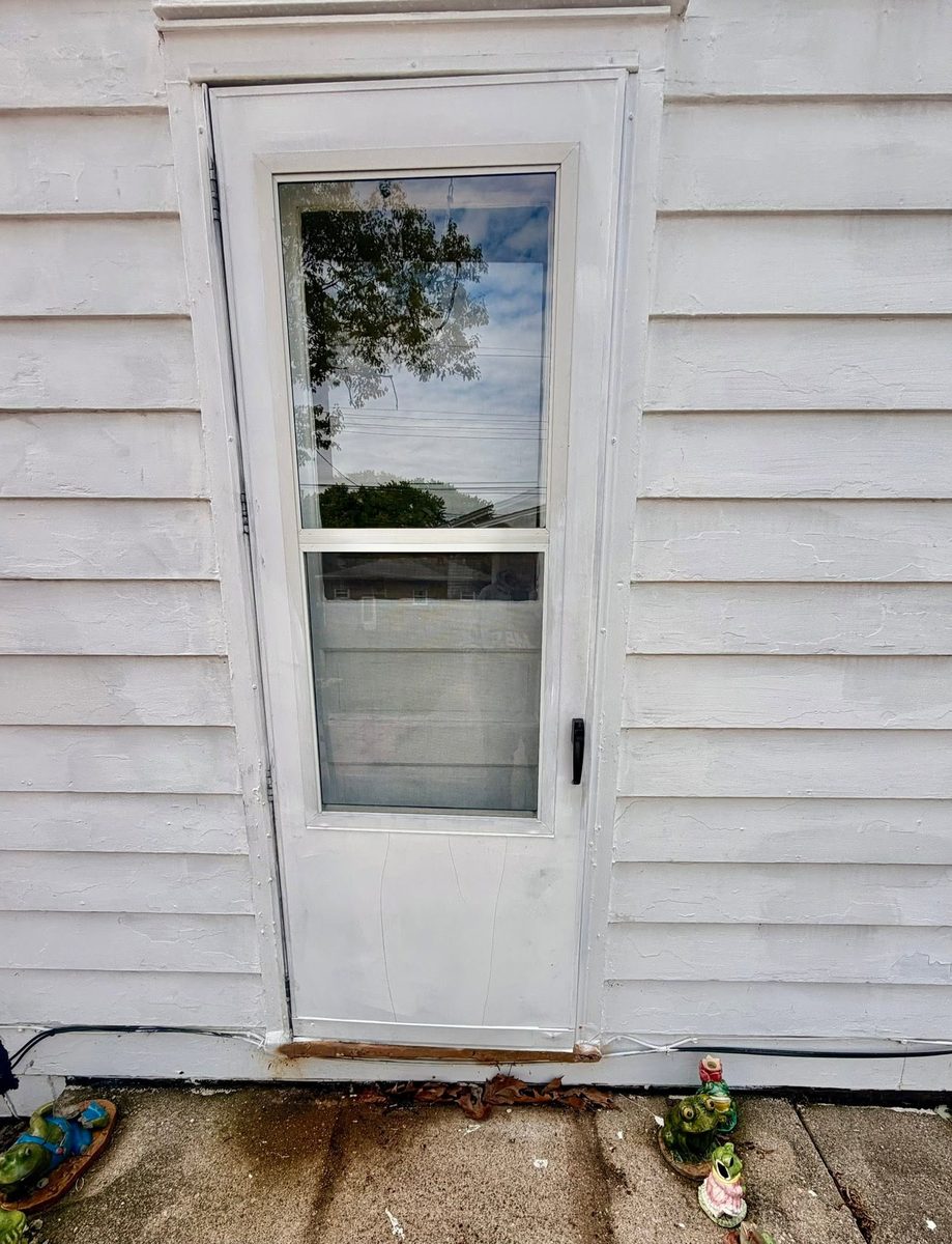 Old white storm door on a clapboard house before replacement