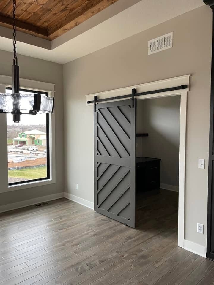 Grey sliding barn door on black track hardware beside a wood plank ceiling