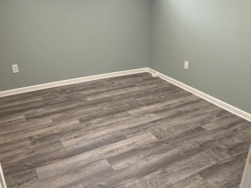 White baseboard installed around a room with grey plank flooring