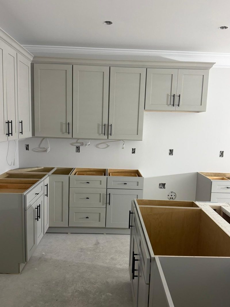 Grey shaker cabinets with crown molding on top and an island carcass mid-install
