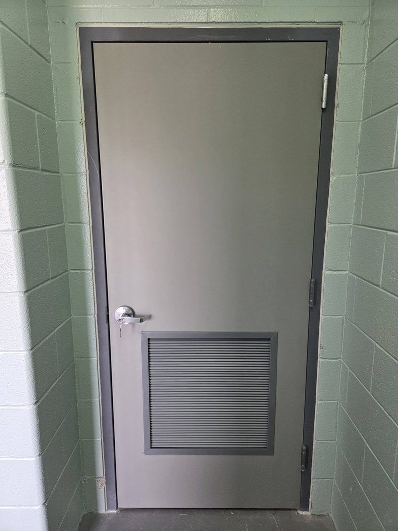 Grey steel door with a louver panel hung in a block wall opening